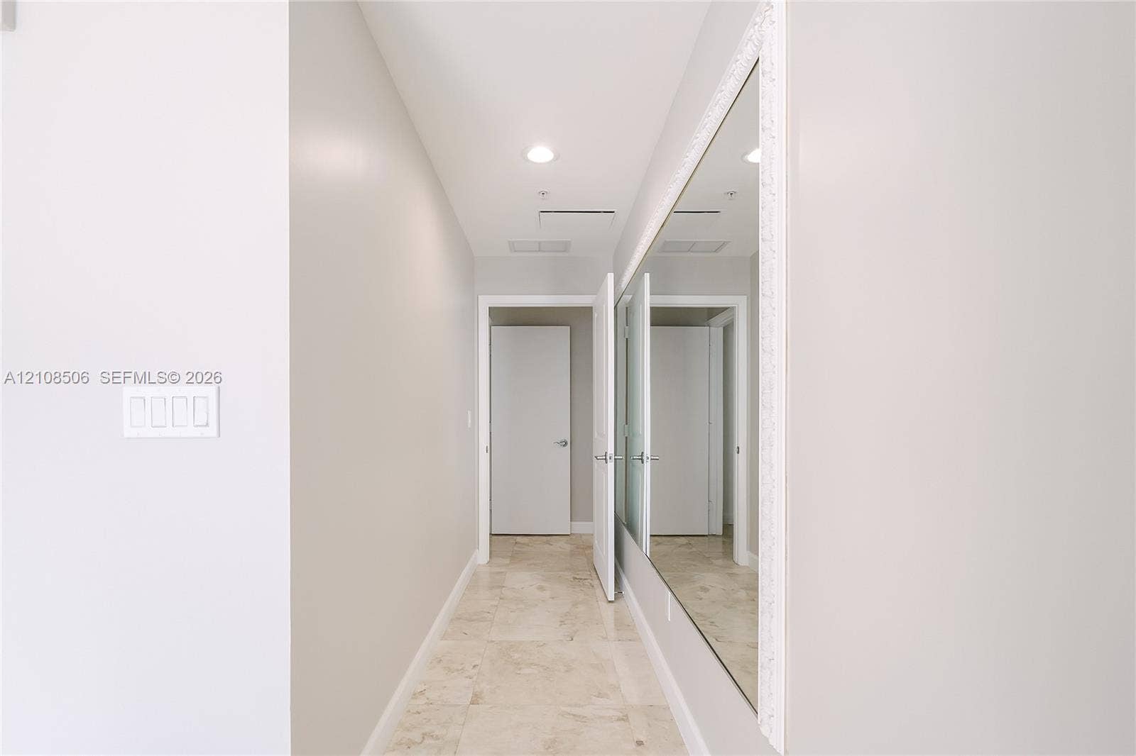 Hallway featuring stone tile flooring, recessed ceiling lighting, and an expansive wall-mounted mirror