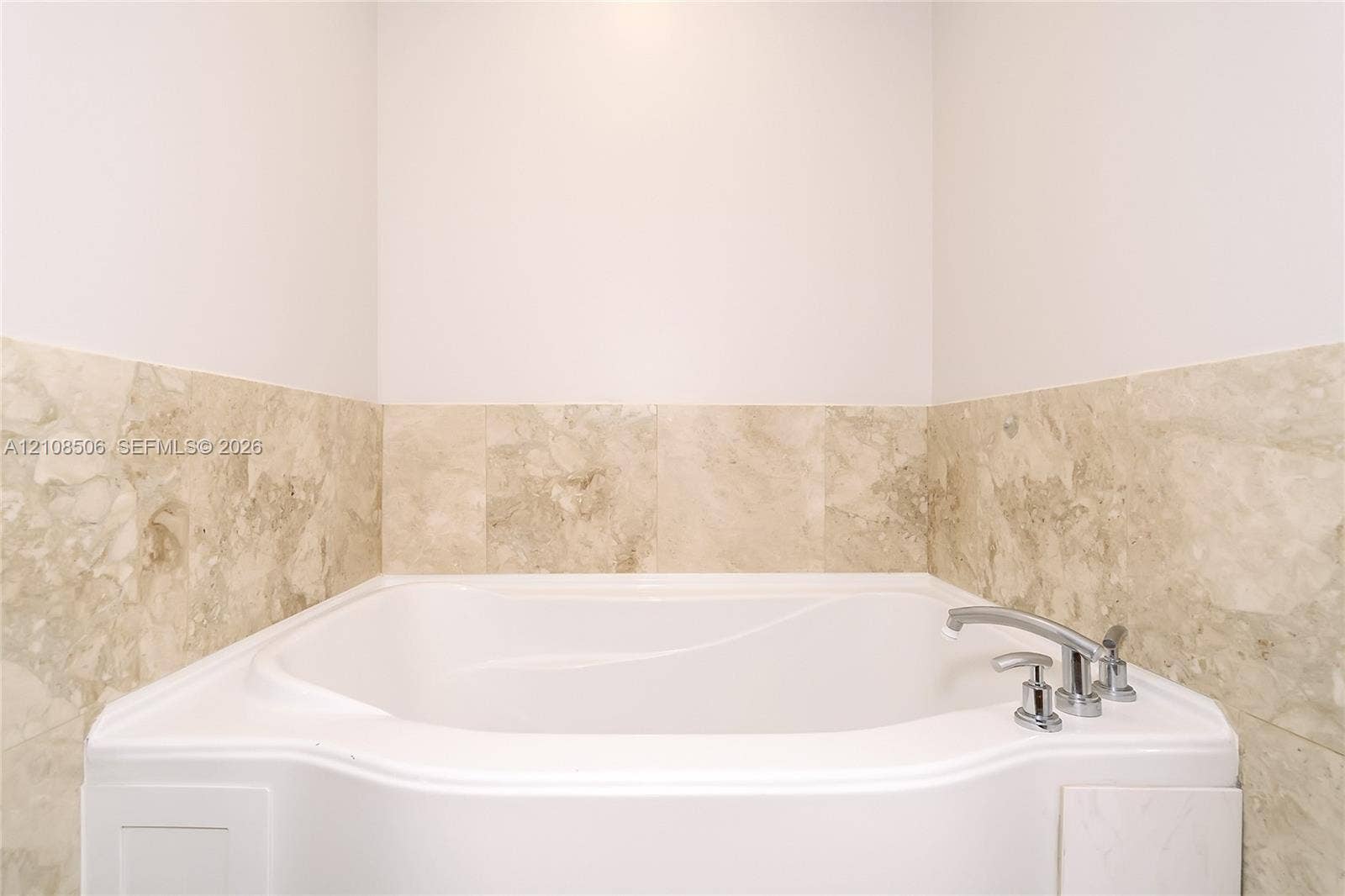 Built-in soaking tub with a polished chrome deck-mounted faucet, surrounded by neutral-toned stone tile wainscoting