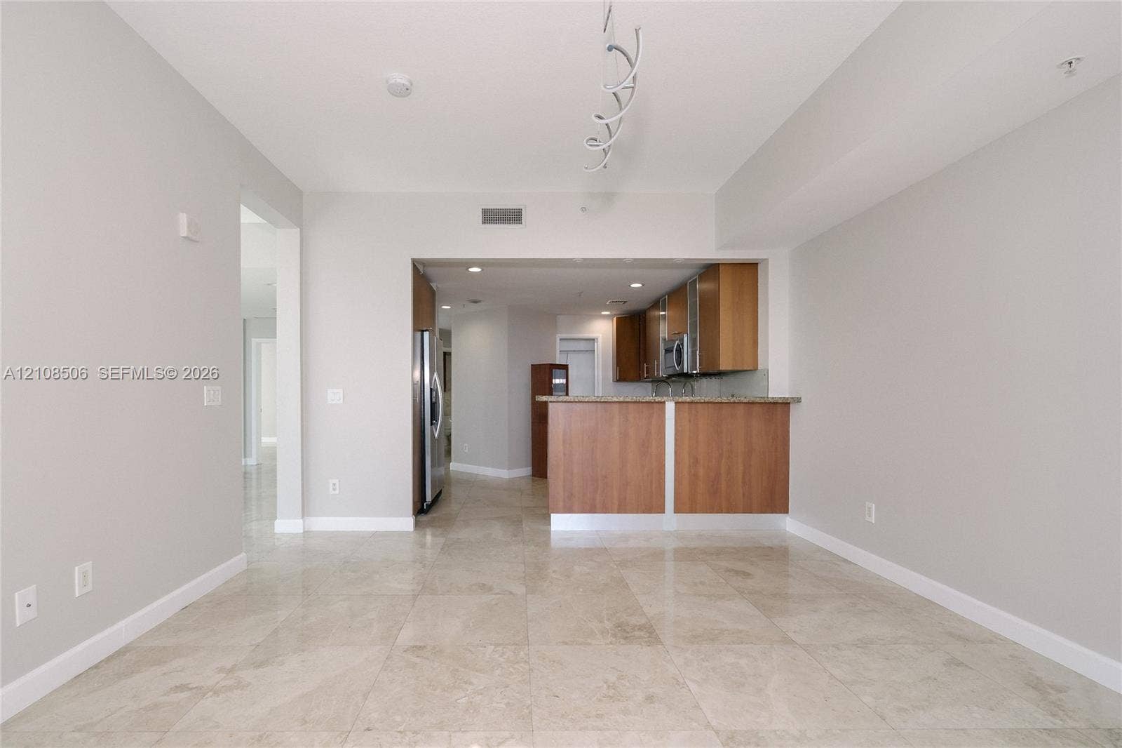 Open concept floor plan featuring light-toned tile flooring, wood-finish cabinetry, a peninsula breakfast bar, and stainless steel appliances