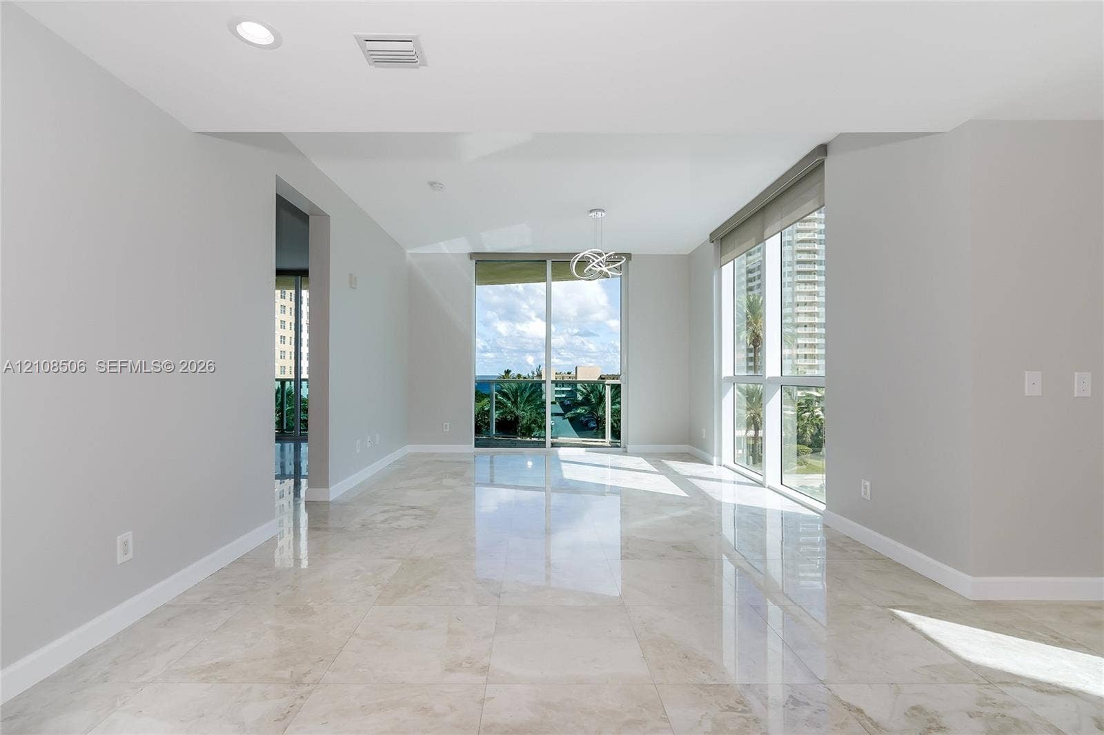 Open-concept room featuring polished stone-finish flooring, floor-to-ceiling windows, recessed lighting, and a modern sculptural pendant fixture