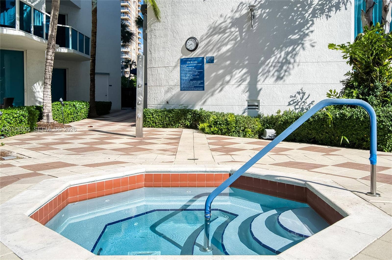 Octagonal in-ground spa featuring a tiled interior, stone coping, a built-in safety handrail, and an exterior shower fixture situated on a paved patio