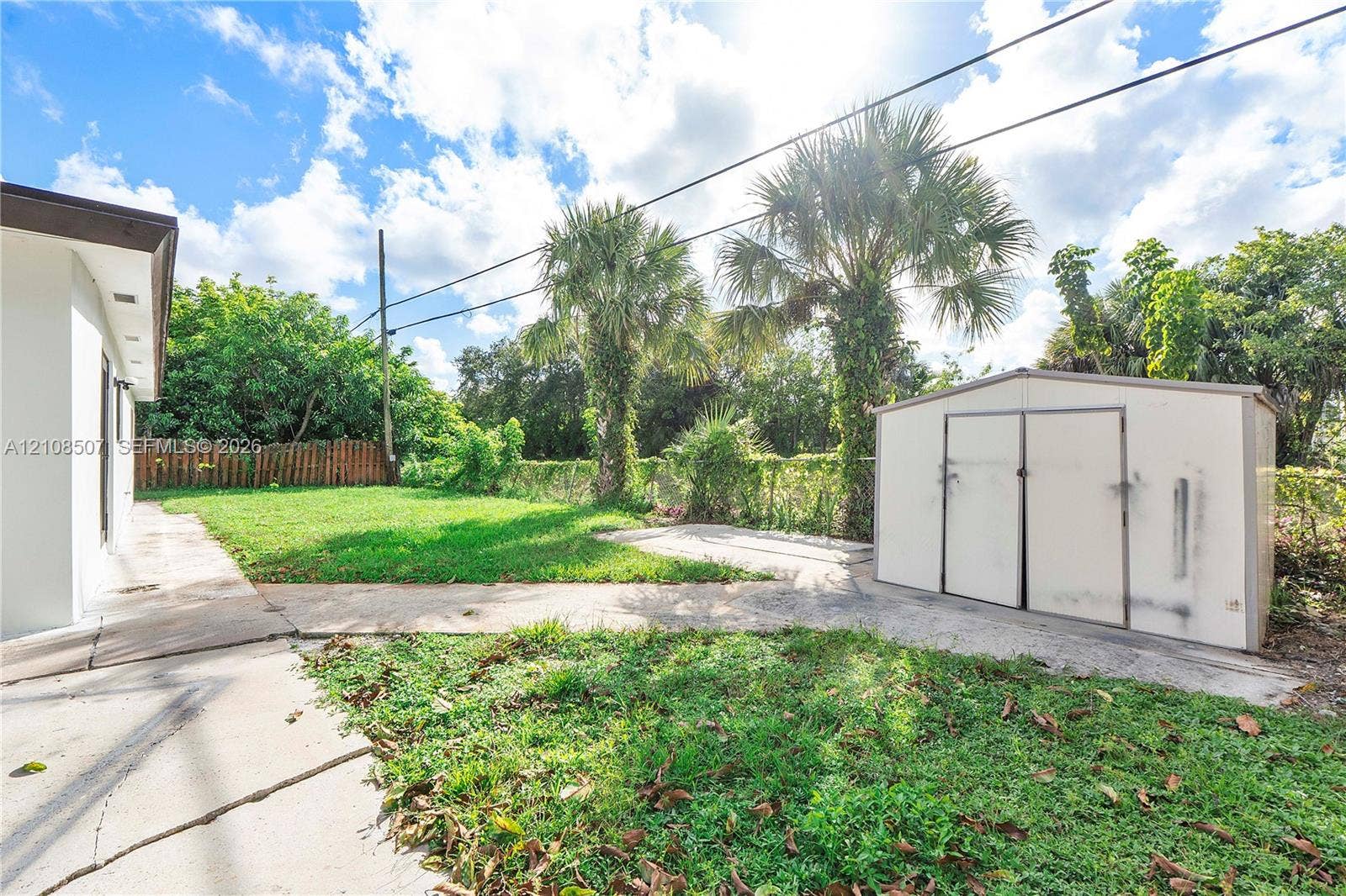 451 SW 38th Terrace, #1, Fort Lauderdale, Fort Lauderdale, FL 33312 Rear exterior featuring a concrete patio, freestanding storage shed, open lawn space, perimeter fencing, and mature palm trees