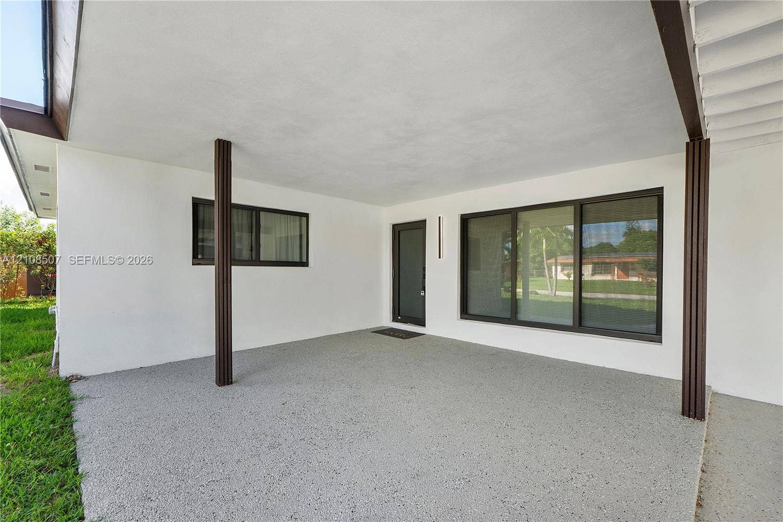 451 SW 38th Terrace, #1, Fort Lauderdale, Fort Lauderdale, FL 33312 Covered patio featuring an aggregate concrete floor, dark-finished structural support columns, a glass-panel entry door, and large-format multi-pane windows with dark frames