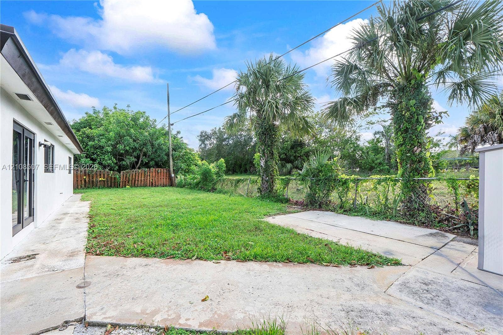 451 SW 38th Terrace, #1, Fort Lauderdale, Fort Lauderdale, FL 33312 Rear exterior featuring a concrete patio, grassy lawn, mature palm trees, and perimeter fencing