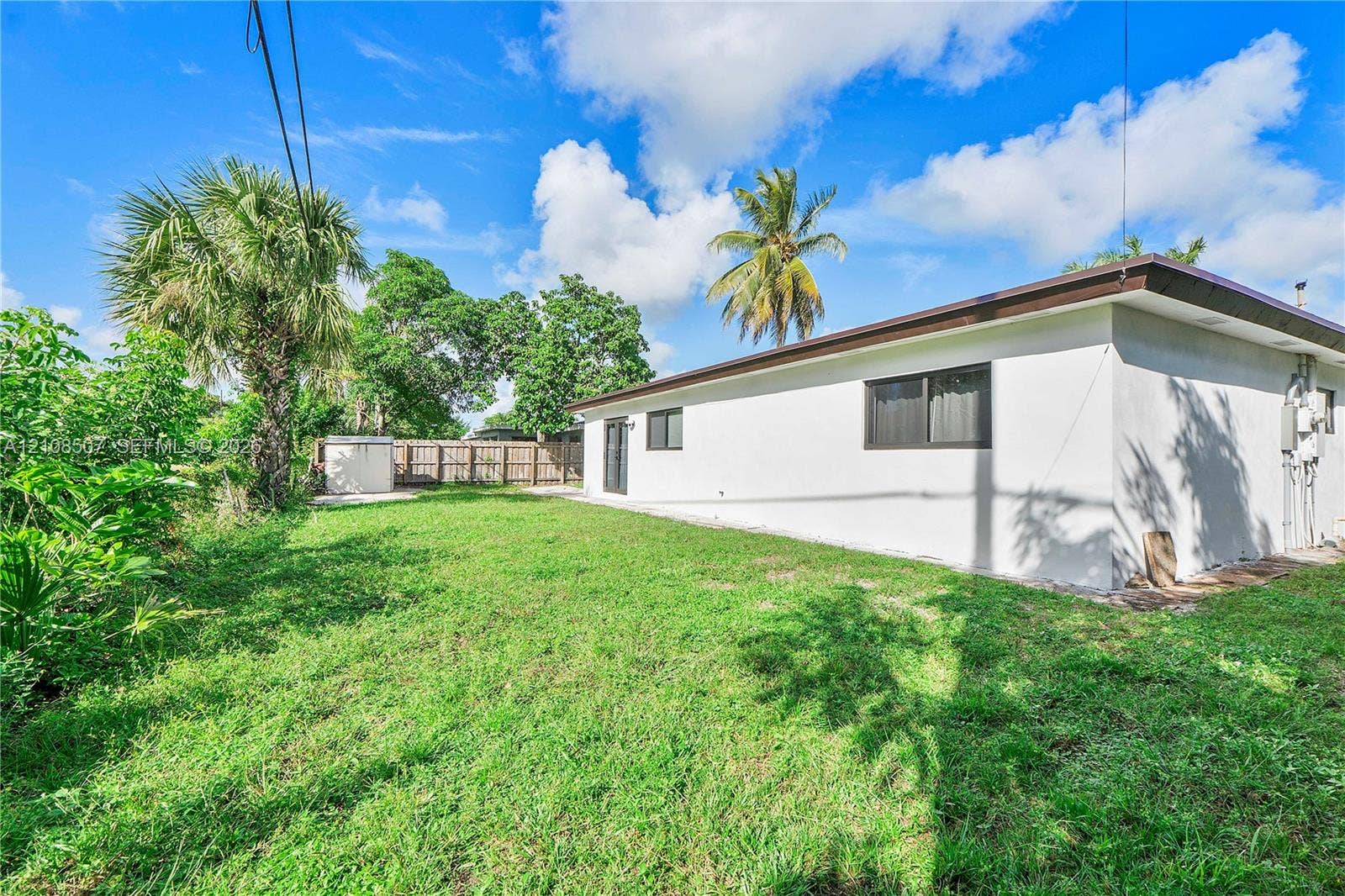 451 SW 38th Terrace, #1, Fort Lauderdale, Fort Lauderdale, FL 33312 Exterior of a single-story residence featuring a smooth stucco facade, dark-framed windows, and a private yard enclosed by wood fencing with mature palm trees