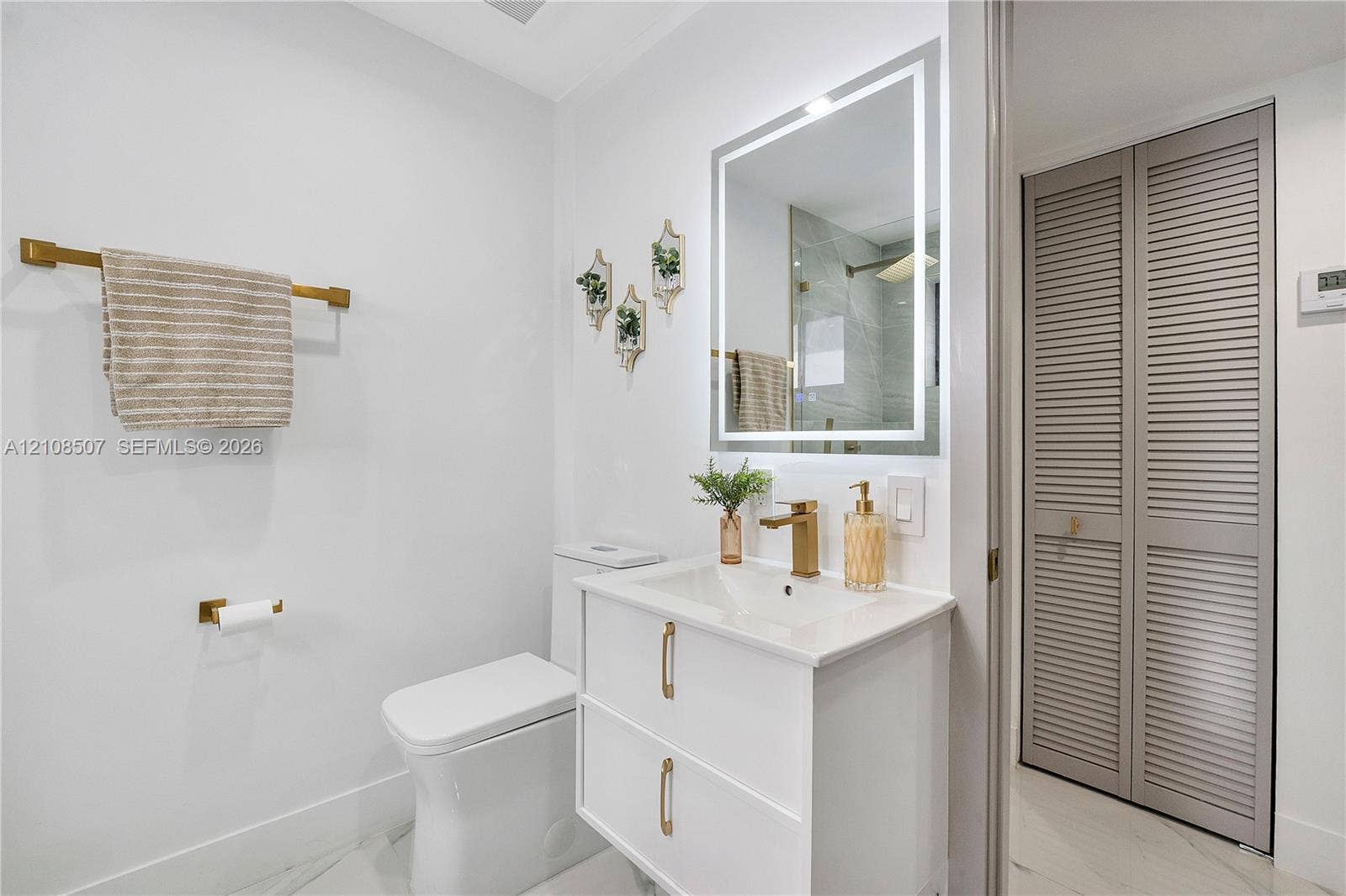 451 SW 38th Terrace, #1, Fort Lauderdale, Fort Lauderdale, FL 33312 White vanity with a rectangular sink, quartz-style countertop, brass-finish faucet and hardware, LED-backlit mirror, and louvered-panel closet doors