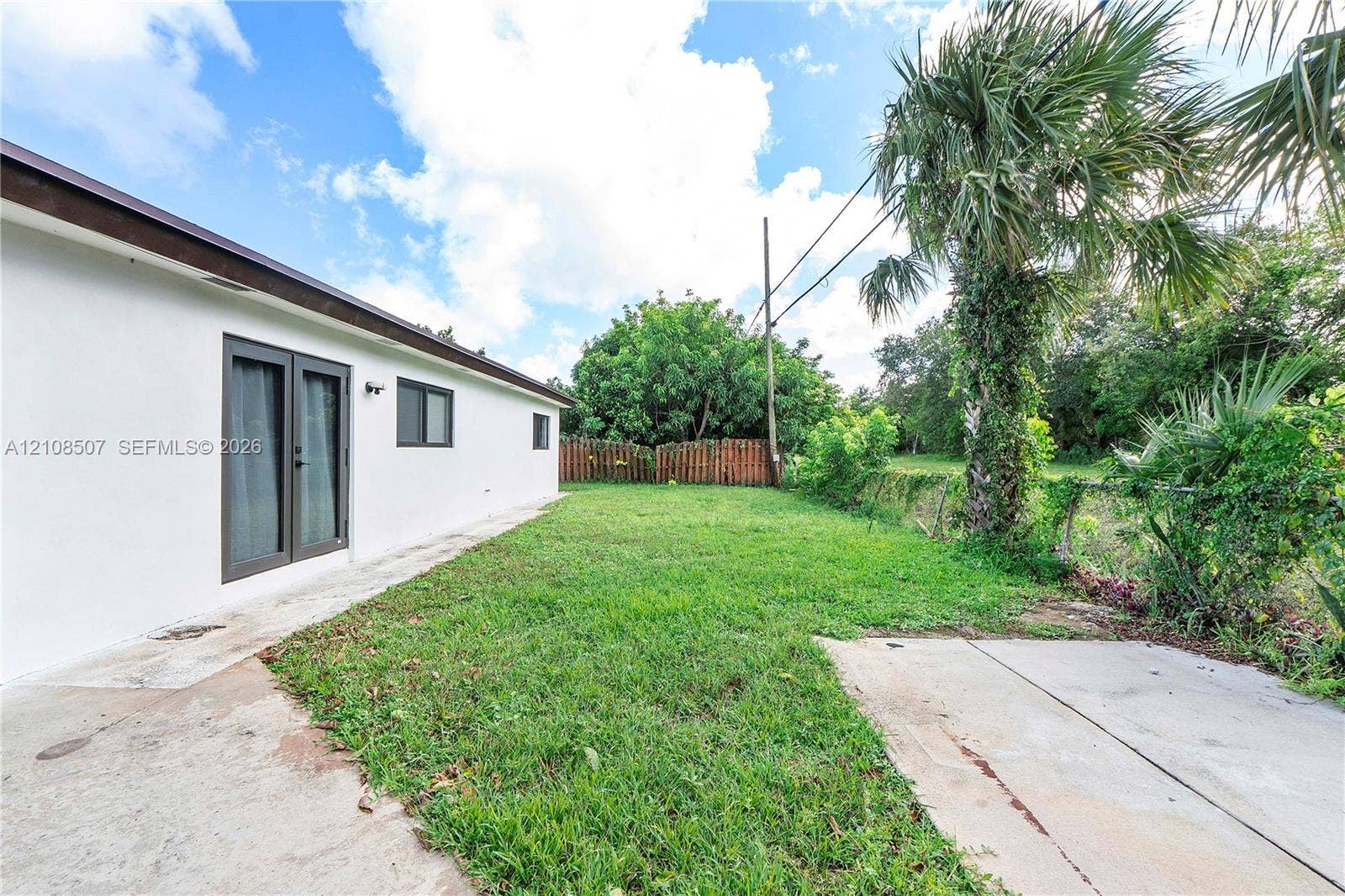 451 SW 38th Terrace, #1, Fort Lauderdale, Fort Lauderdale, FL 33312 Exterior side yard featuring white stucco siding, double-pane glass French doors, a concrete patio, and mature palm landscaping