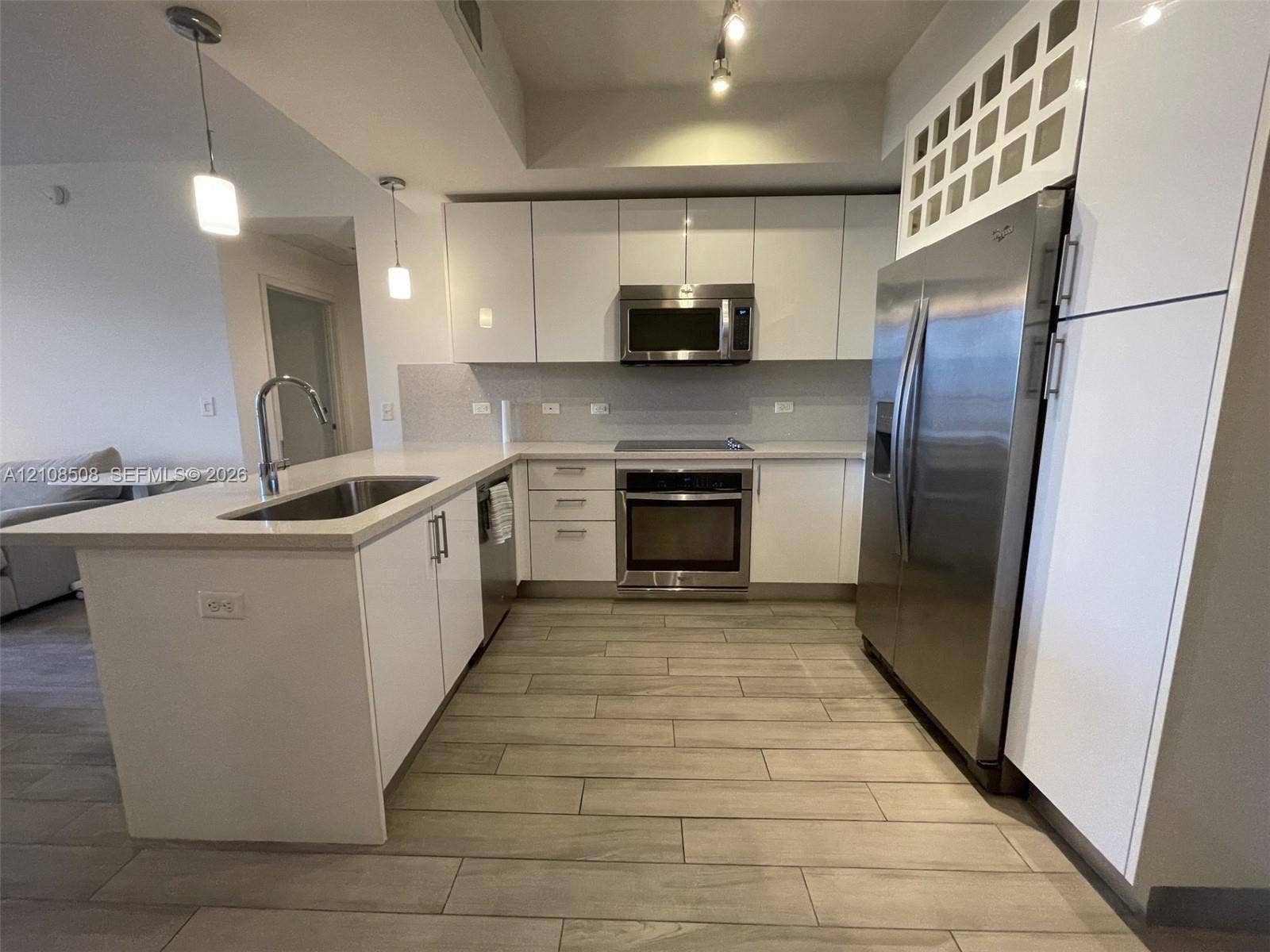 Kitchen featuring high-gloss white cabinetry, stone-surface countertops, stainless steel appliances, pendant lighting, and wood-finish tile flooring