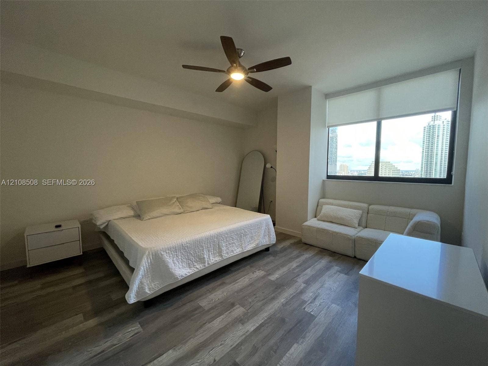Wood-finish flooring, ceiling fan with integrated lighting, expansive window with roller shade, and neutral wall tones