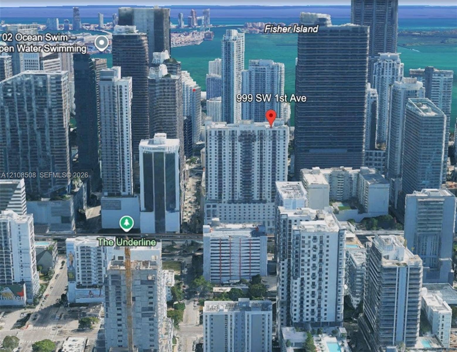 Aerial perspective of a high-rise residential building situated within a dense urban metropolitan center, featuring proximity to coastal waterways and developed city infrastructure