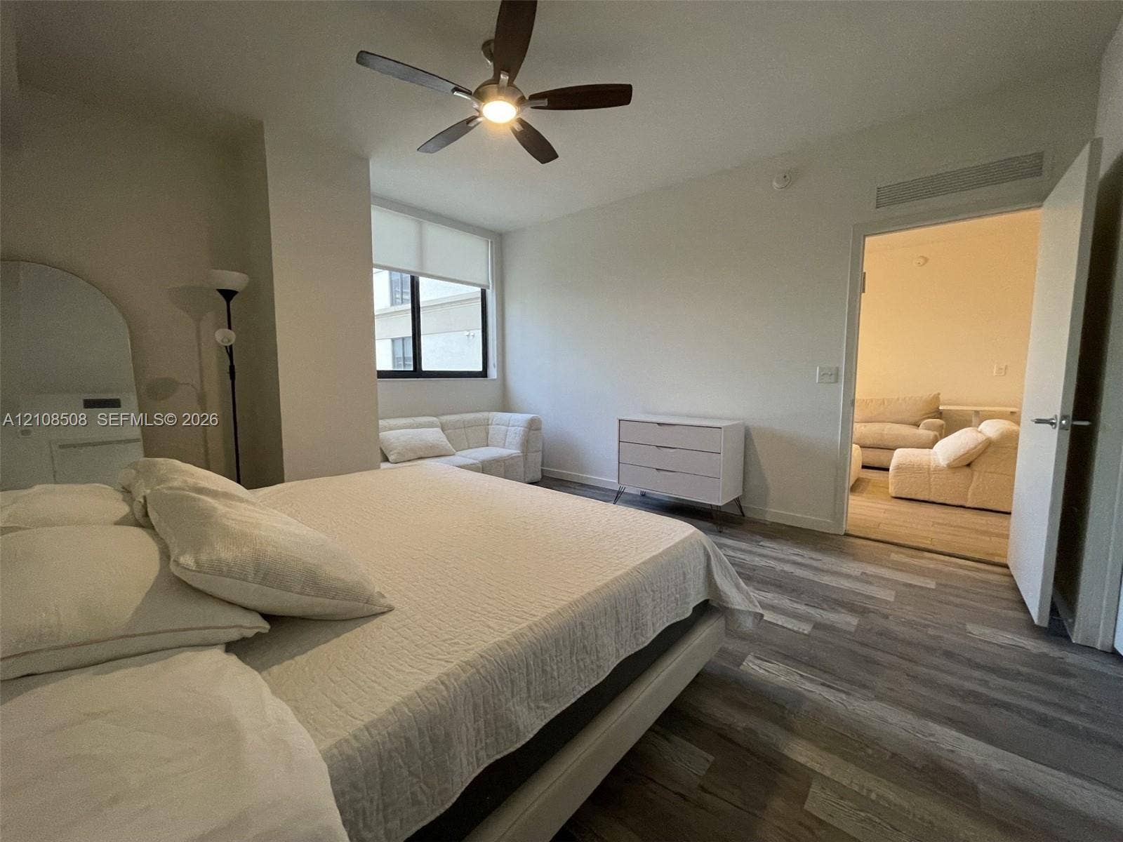 Room featuring wood-finish flooring, a multi-blade ceiling fan with integrated lighting, and a window with a fitted roller shade