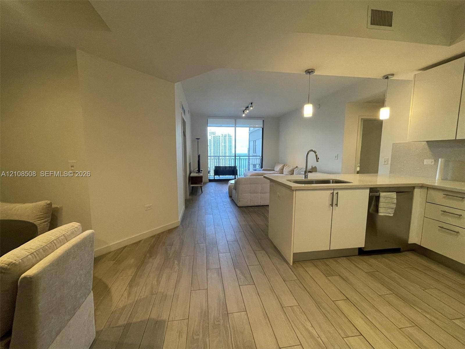 Kitchen featuring white cabinetry, solid-surface countertops, and stainless steel dishwasher, with wood-finish flooring throughout the space and floor-to-ceiling glass paneling