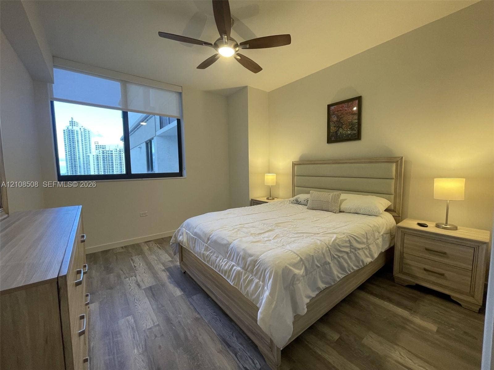 Wood-finish flooring, large-format window with roller shade, and ceiling-mounted fan with integrated lighting