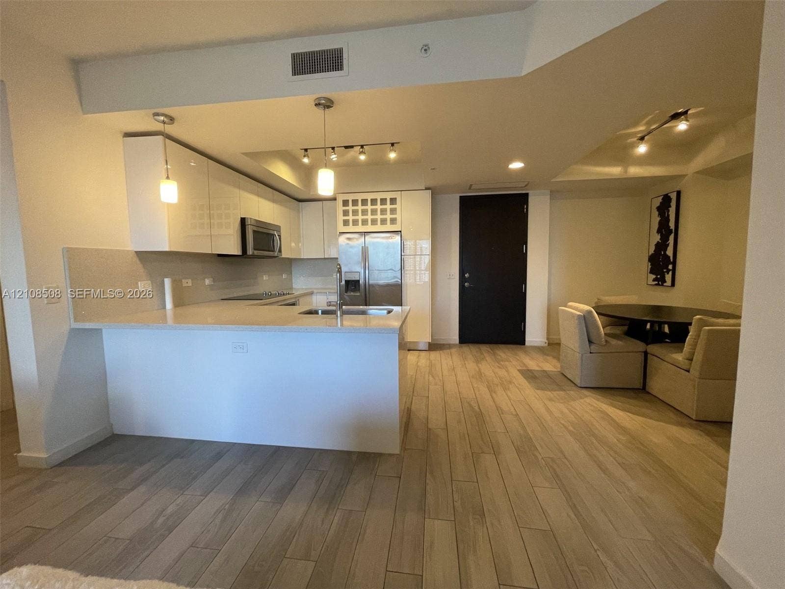 Kitchen featuring high-gloss white cabinetry, stone-finish countertops, stainless steel appliances, wood-finish flooring, and recessed track lighting