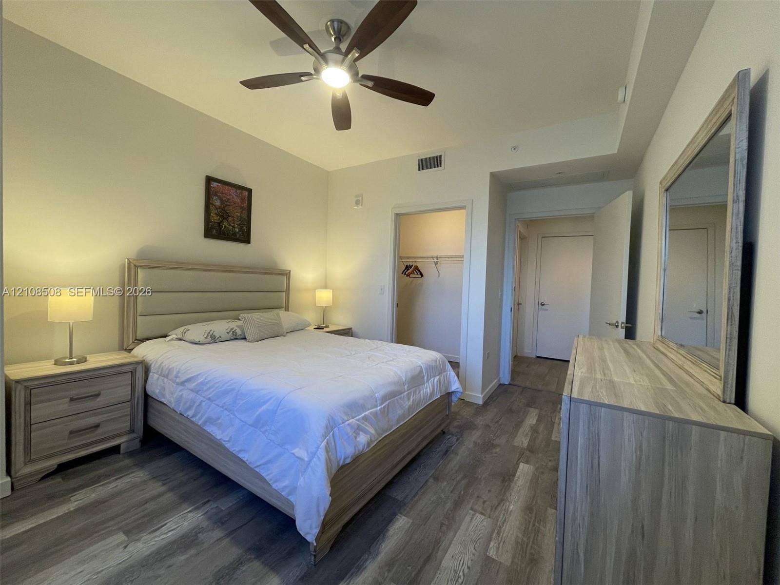 Neutral-toned interior featuring wood-finish flooring, a multi-blade ceiling fan, and a walk-in closet with built-in shelving