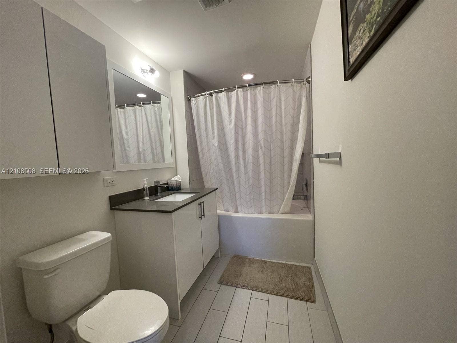 Bathroom featuring a vanity with dark countertop, rectangular integrated sink, tall storage cabinetry, and a bathtub with tile surround