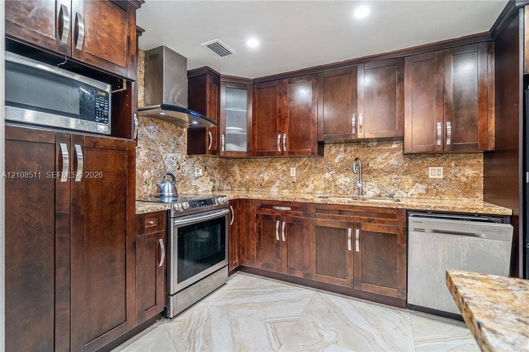 Miramar, Miramar, FL 33025 Kitchen featuring dark wood cabinetry, stone countertops, stone backsplash, stainless steel appliances, and large-format tile flooring