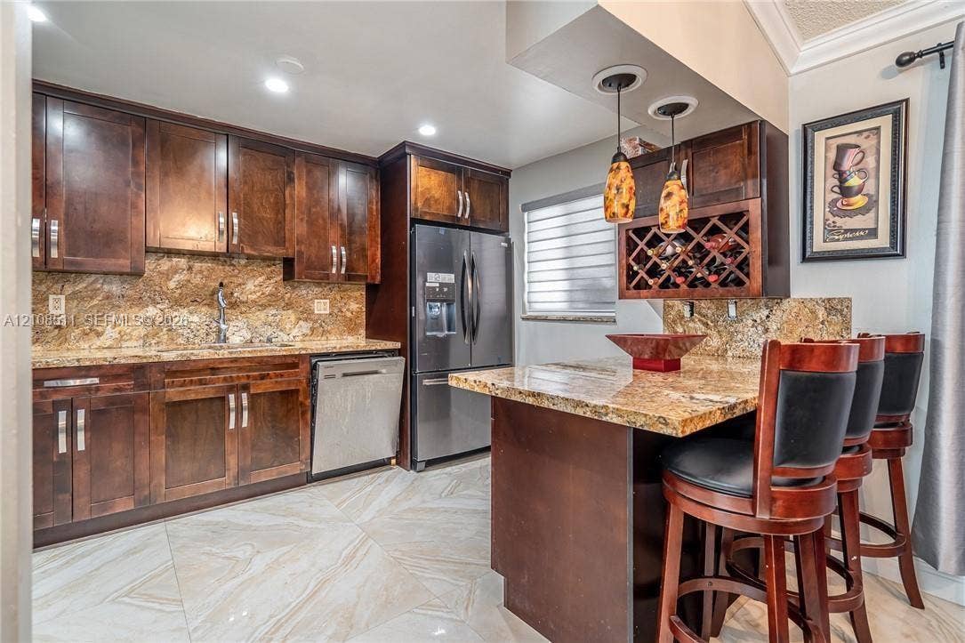 Miramar, Miramar, FL 33025 Kitchen featuring dark wood cabinetry, natural stone countertops, a built-in wine rack, dual pendant lighting, and large-format tile flooring