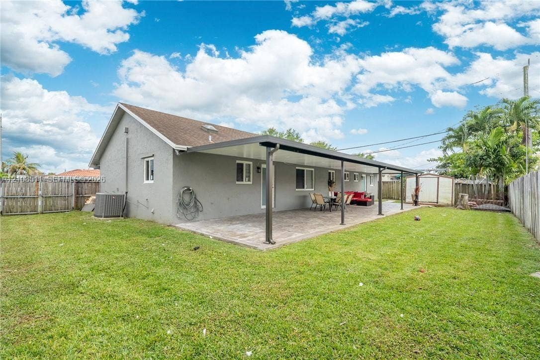 Miramar, Miramar, FL 33025 Spacious backyard featuring a covered patio, paved hardscaping, wood-style privacy fencing, and exterior storage structure