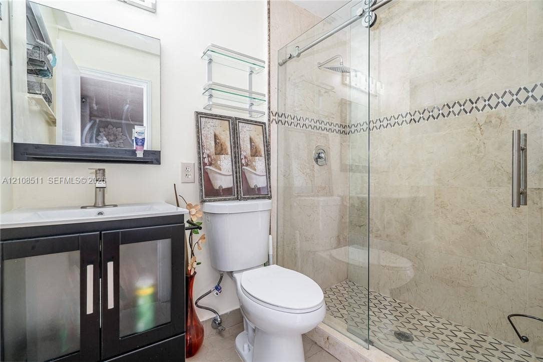 Miramar, Miramar, FL 33025 Bathroom featuring a vanity with frosted glass cabinet doors, a rectangular sink, a shower enclosure with sliding glass doors, stone wall tile, and a geometric patterned tile shower floor