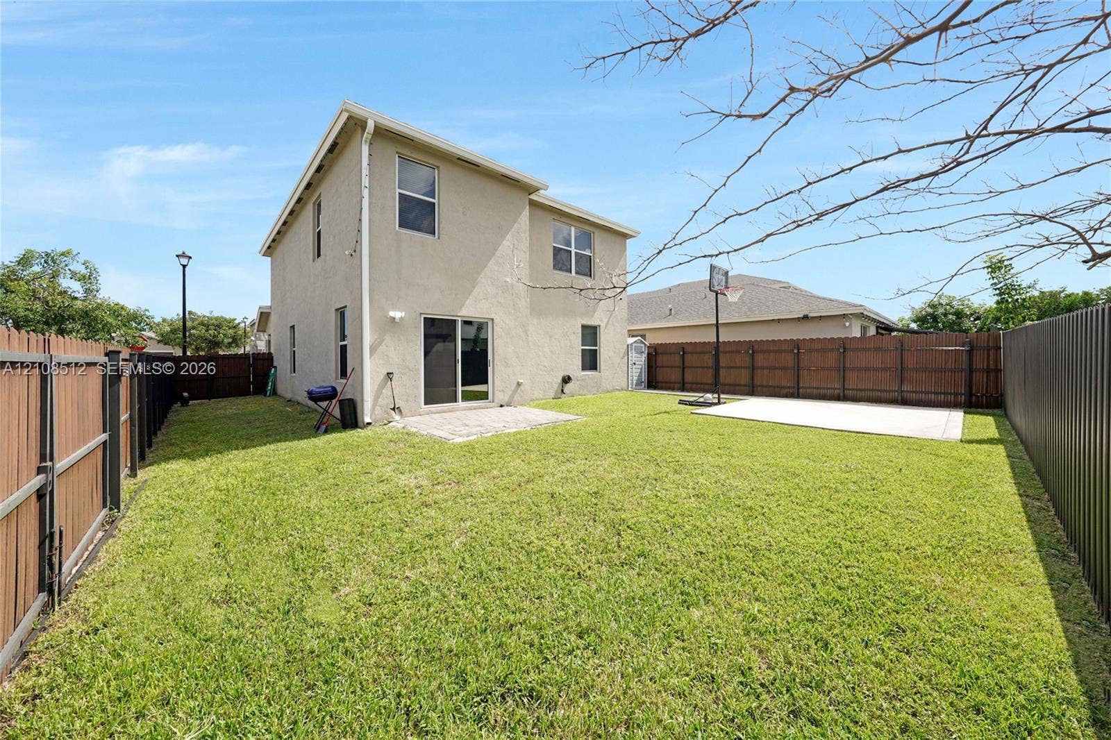 Backyard featuring a stucco exterior, concrete patio, grass lawn, and wood-panel privacy fencing