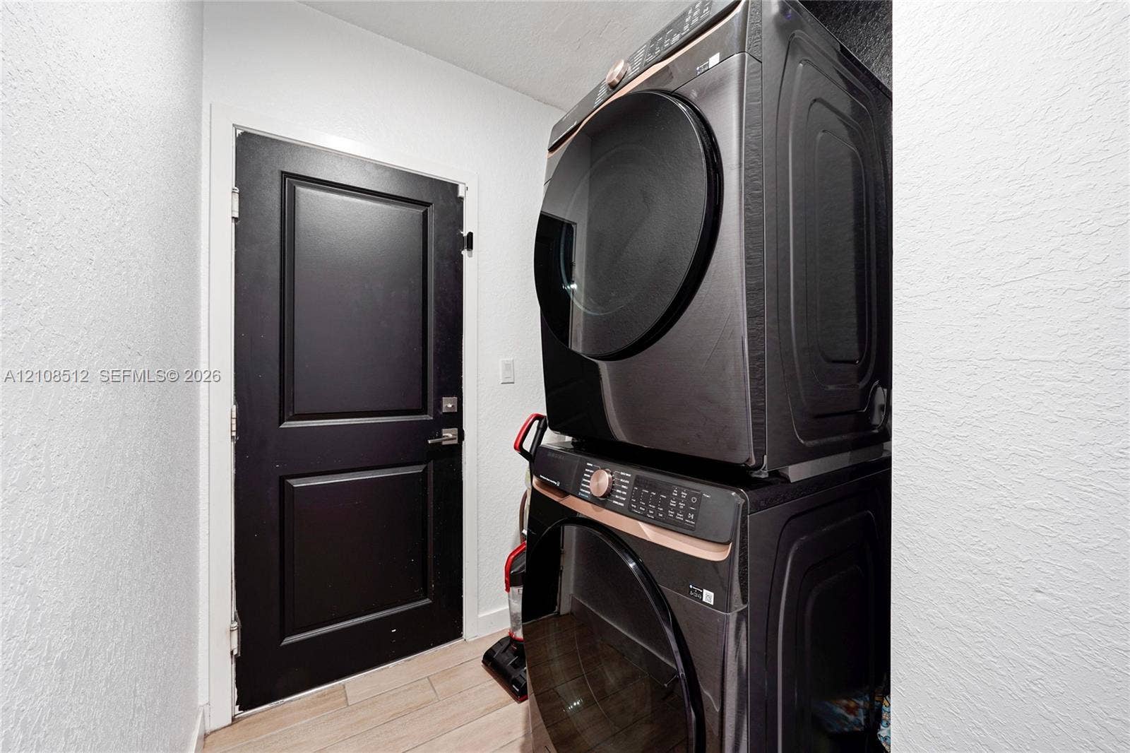 Laundry area featuring a stacked washer and dryer unit, wood-finish tile flooring, and a solid-core black interior door with matching hardware