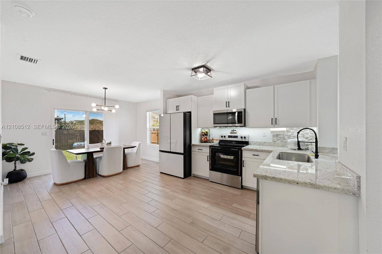 Kitchen featuring white shaker-style cabinetry, stone-finish countertops, stainless steel appliances, wood-finish tile flooring, and a multi-light fixture