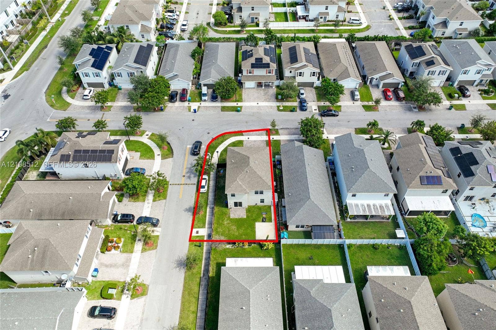 Aerial perspective of a corner lot property featuring a hip roof, paved driveway, dedicated rear patio, and expansive side lawn