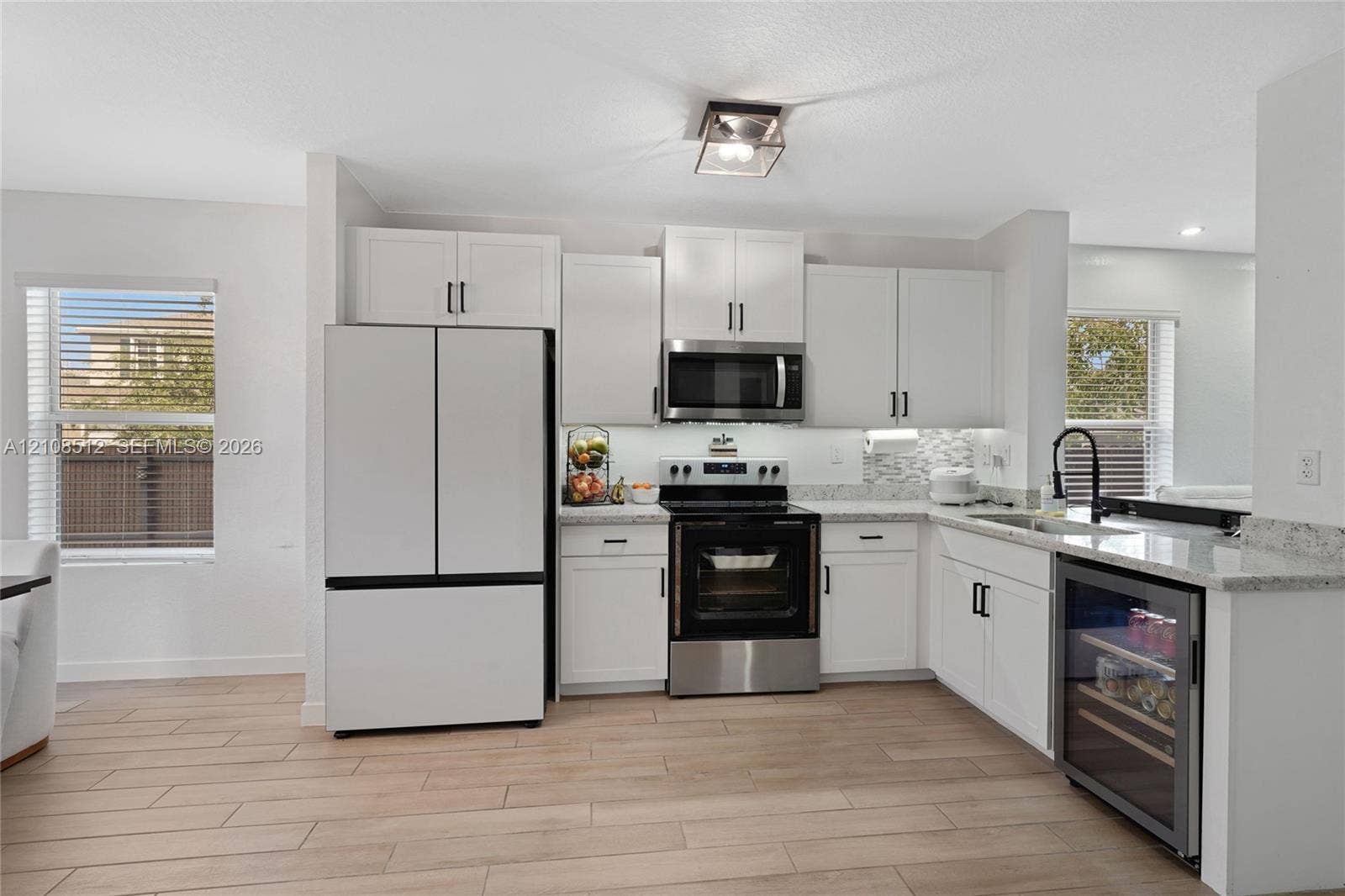 Kitchen featuring white shaker-style cabinetry, stone-surface countertops, stainless steel appliances, a built-in wine refrigerator, and wood-finish tile flooring