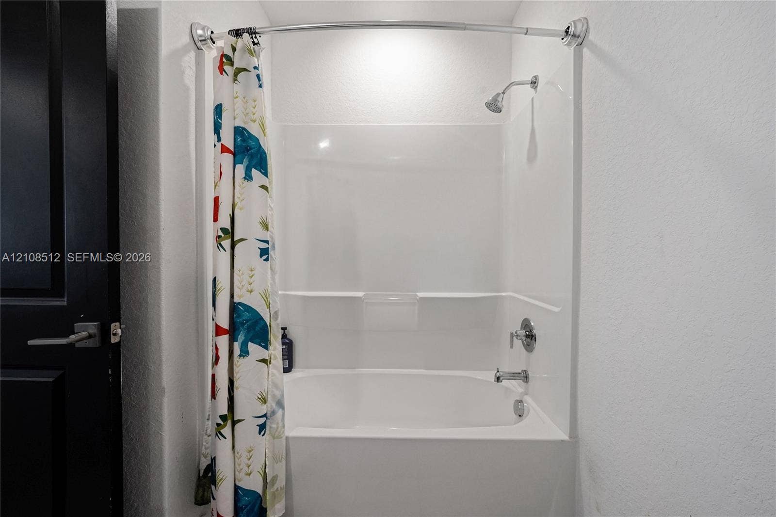 Bathtub and shower combination with a white acrylic surround, integrated shelving, a polished chrome faucet, and a wall-mounted shower head