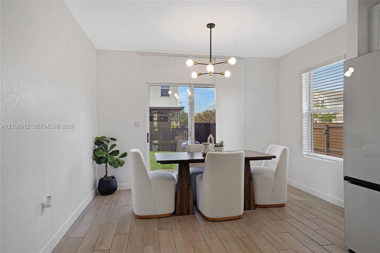 Dining area featuring wood-finish flooring, a modern six-light chandelier, a large window, and a sliding glass door providing external access