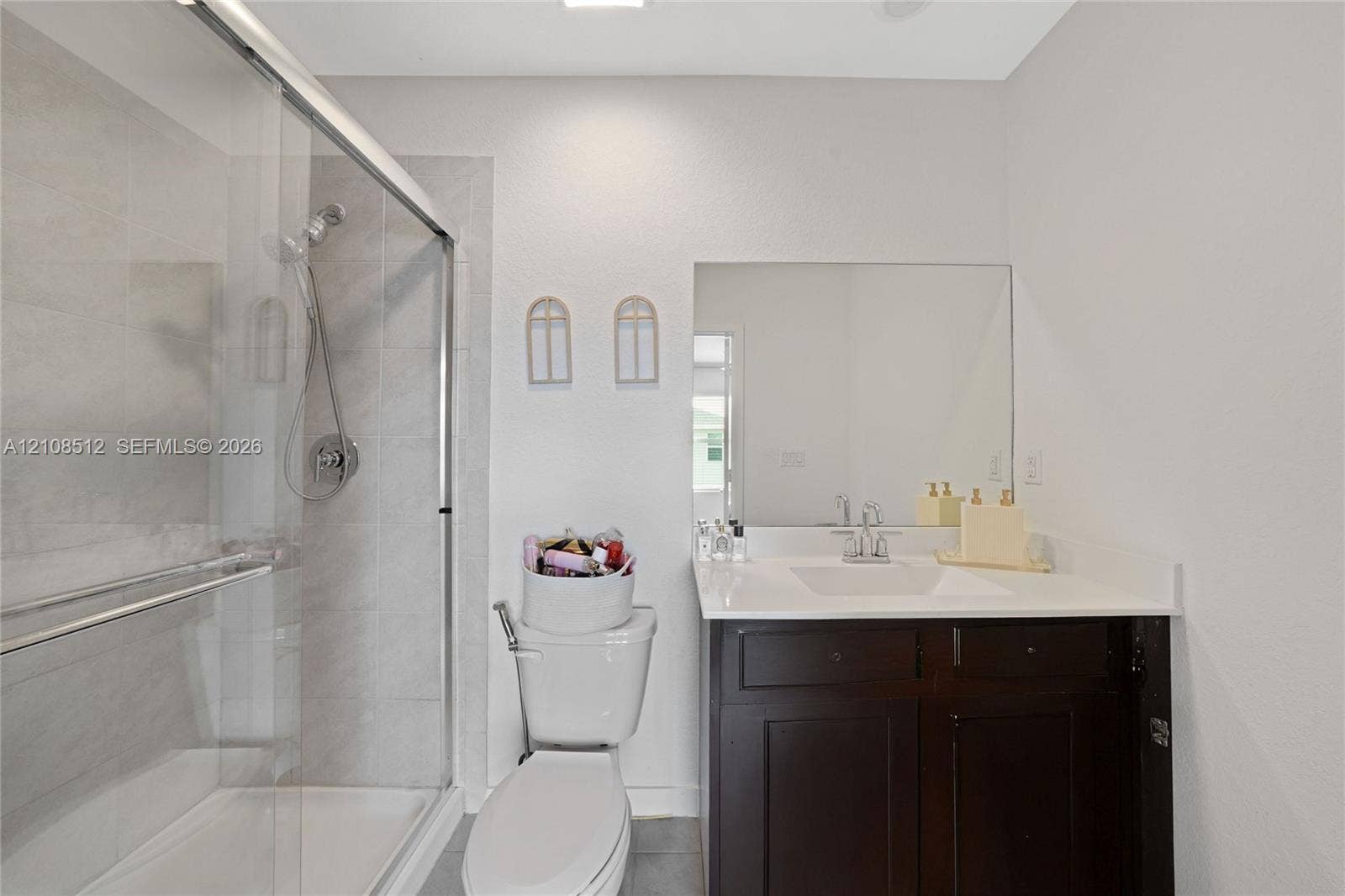 Bathroom featuring a dark wood-finish vanity with a stone countertop, an integrated rectangular sink, a glass-enclosed shower with tiled surround, and a large wall-mounted mirror