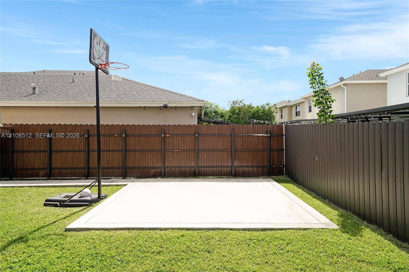 Private backyard featuring a concrete sport court, perimeter wood privacy fencing, and metal panel fencing