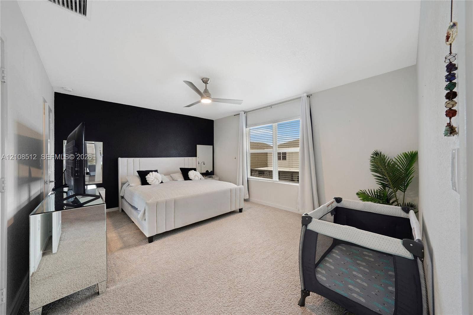 Bedroom featuring vaulted ceilings, a prominent accent wall, neutral carpeting, and a ceiling fan with integrated lighting