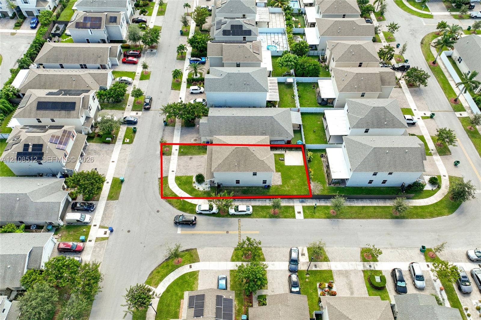 Aerial view of a corner lot property featuring a hip roof, exterior concrete walkway, paved ground-level patio, and lawn space