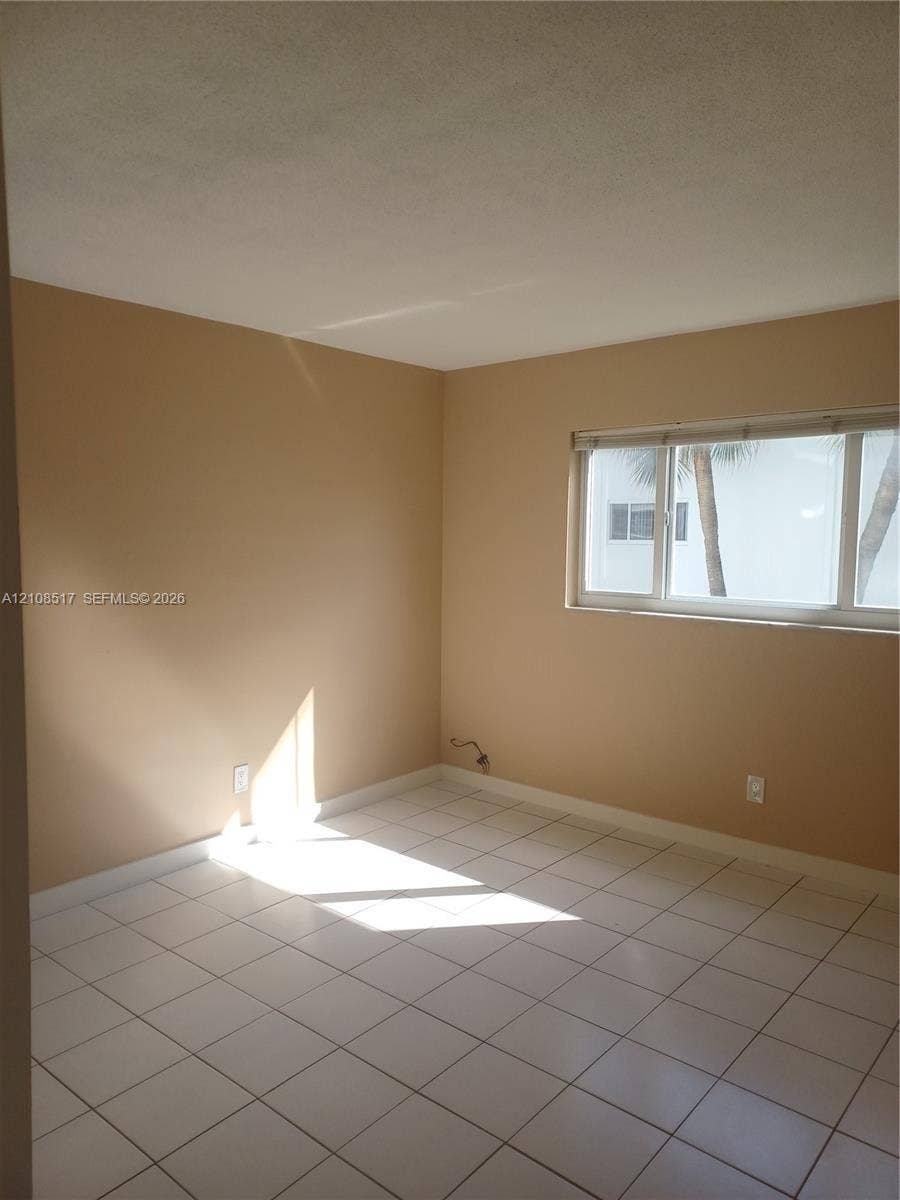 541 Blue Heron Drive, #204, Hallandale Beach, FL 33009 Neutral-toned interior space featuring light-colored ceramic tile flooring, horizontal window blinds, and natural light exposure