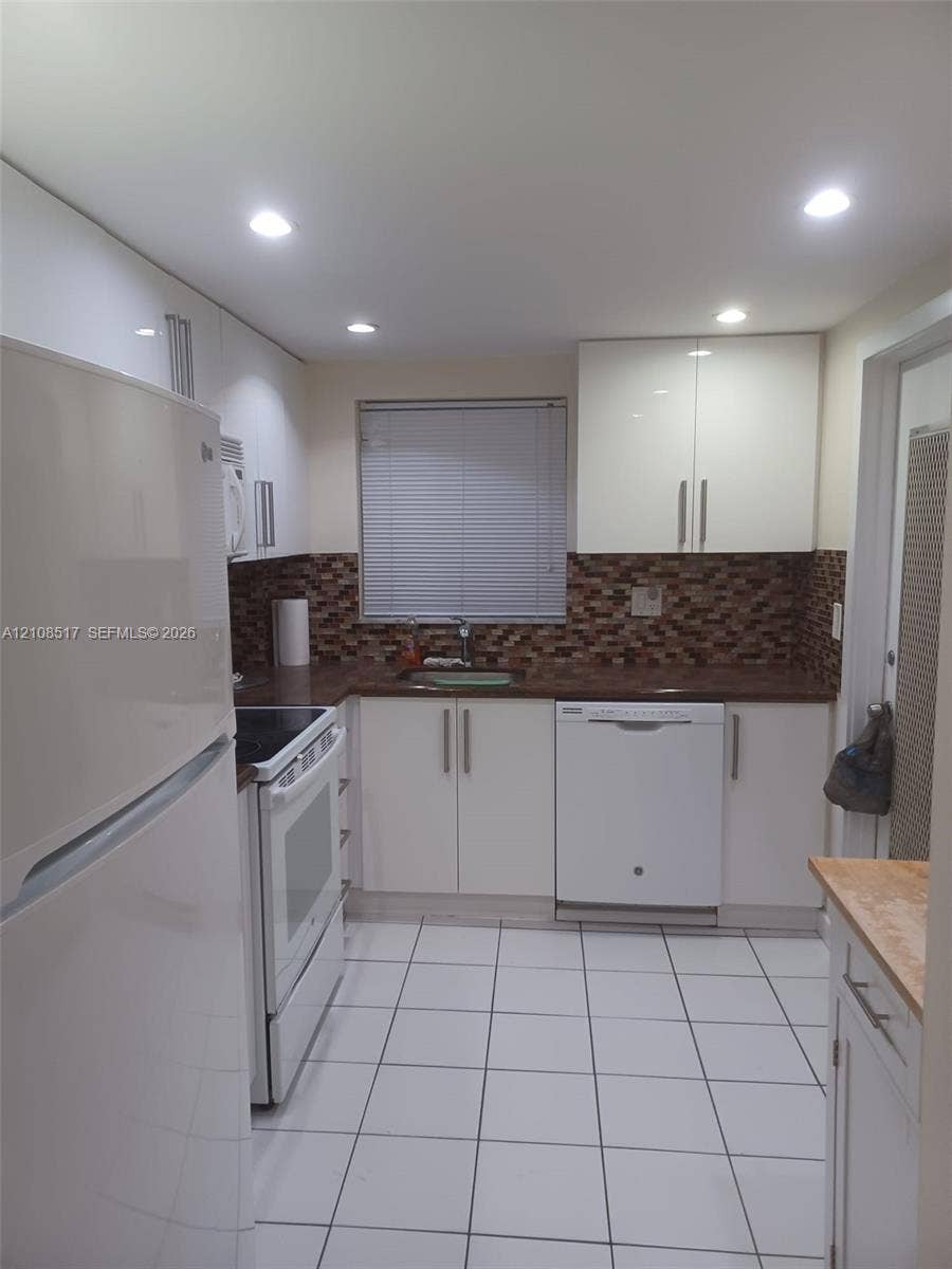 541 Blue Heron Drive, #204, Hallandale Beach, FL 33009 Kitchen featuring high-gloss white cabinetry, white ceramic tile flooring, a mosaic tile backsplash, and recessed ceiling lighting