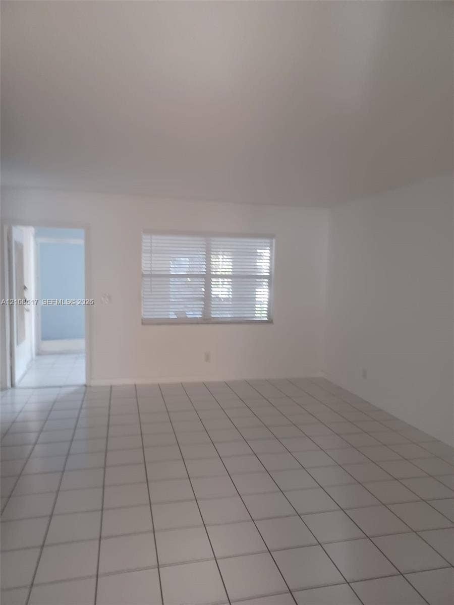 541 Blue Heron Drive, #204, Hallandale Beach, FL 33009 Neutral-toned interior space featuring white walls, large-format ceramic tile flooring, and a multi-pane window with horizontal blinds