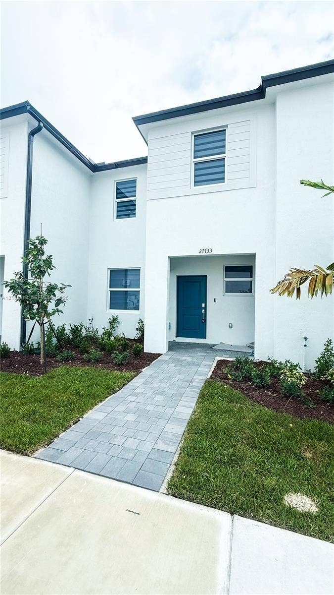 27733 SW 155th Court, #27733, Homestead, Homestead, FL 33032 Contemporary exterior featuring a white smooth-stucco facade, a solid blue entry door, multi-pane windows, and a paved stone walkway