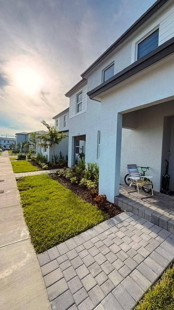 27733 SW 155th Court, #27733, Homestead, Homestead, FL 33032 Exterior facade featuring light-toned stucco and horizontal siding, covered entryway with paver flooring, and landscaped front yard with turf and mulch beds