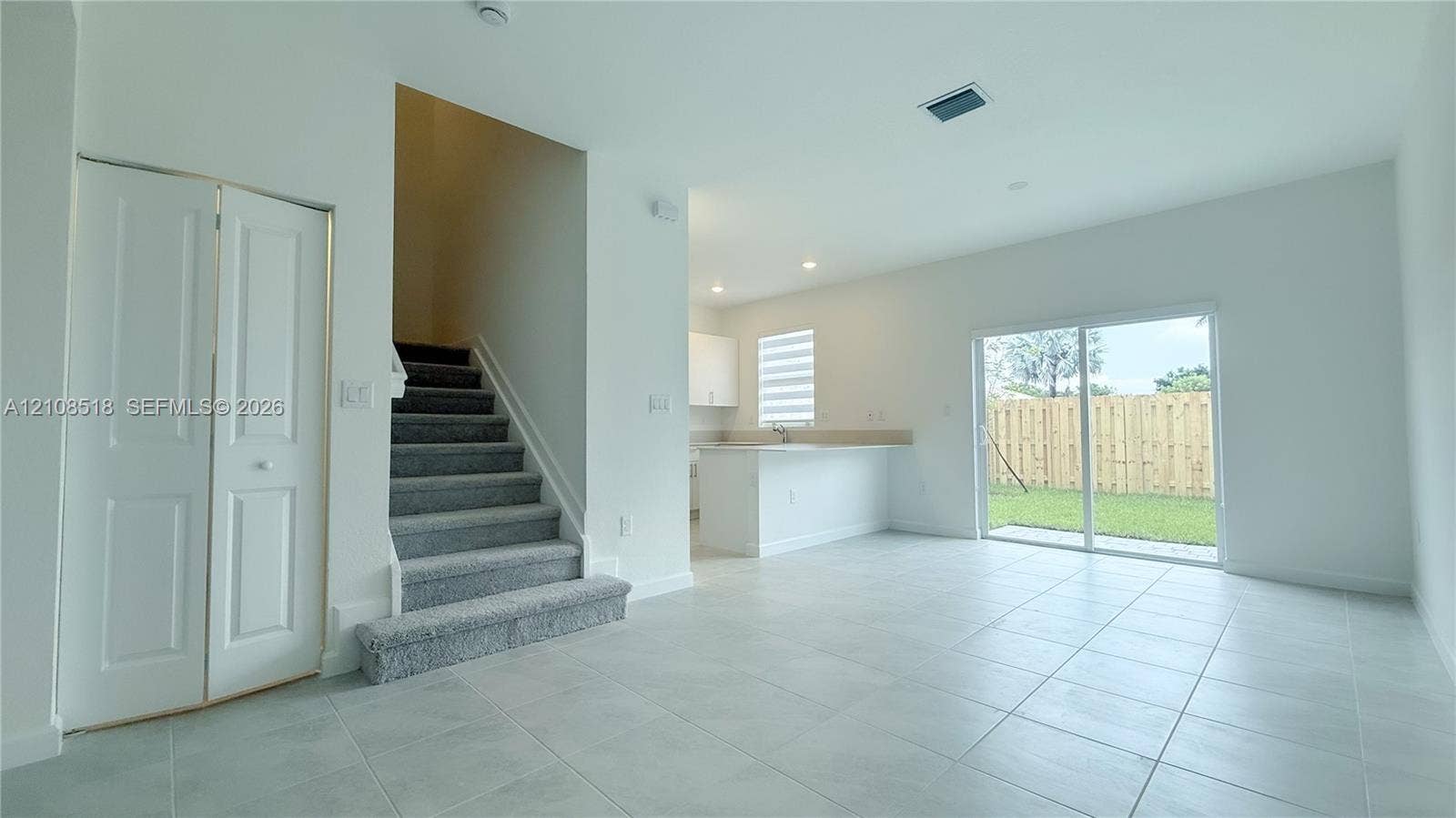 27733 SW 155th Court, #27733, Homestead, Homestead, FL 33032 Open-concept interior featuring neutral tile flooring, carpeted staircase with white railings, sliding glass doors, built-in storage closet, and kitchen peninsula