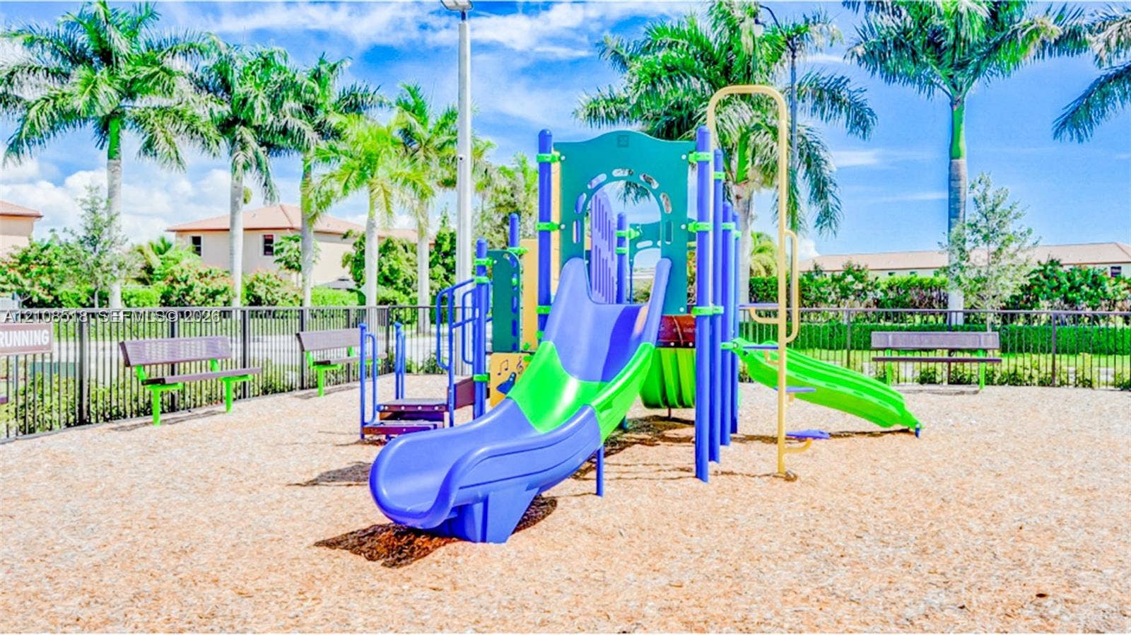 27733 SW 155th Court, #27733, Homestead, Homestead, FL 33032 Community playground featuring a multi-level structure with slides, integrated benches, and palm-lined landscaping, set within a fenced area with wood chip ground cover