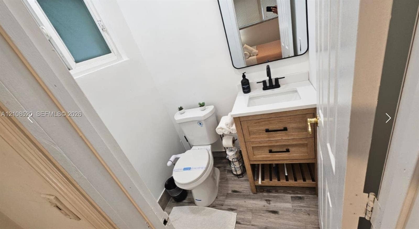 4536 SW 24th Avenue, Dania, Dania Beach, FL 33312 Bathroom featuring a wood-finish vanity with a white countertop and rectangular sink, matte black faucet, rectangular mirror with a black frame, and wood-finish flooring