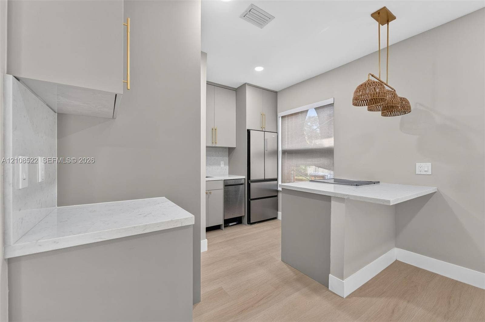 Kitchen featuring light grey cabinetry with gold-tone hardware, white stone-finish countertops, stainless steel appliances, and light wood-finish flooring