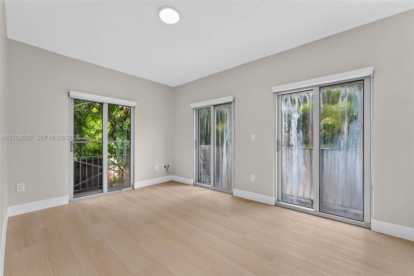 Neutral-toned interior featuring wood-finish flooring, three sliding glass doors, and recessed ceiling lighting