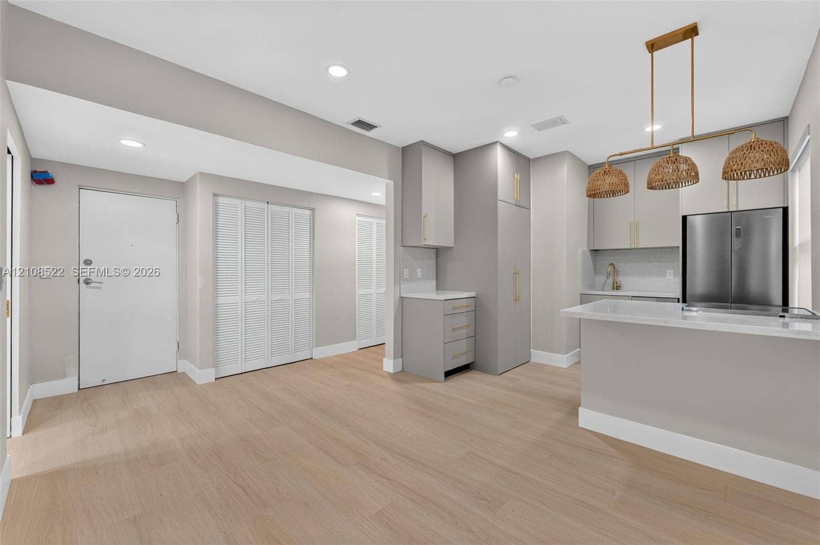Kitchen featuring wood-finish flooring, custom cabinetry with brushed gold hardware, quartz countertops, a multi-pendant woven light fixture, and built-in stainless steel appliances
