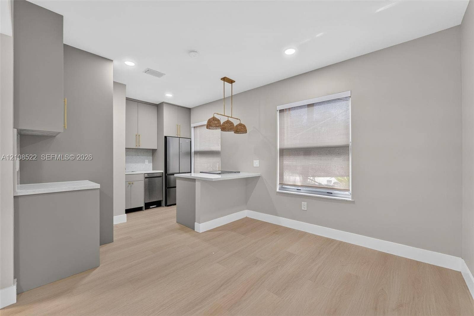 Kitchen featuring wood-finish flooring, matte-finish cabinetry, stone-surfaced countertops, stainless steel appliances, and multi-pendant overhead lighting
