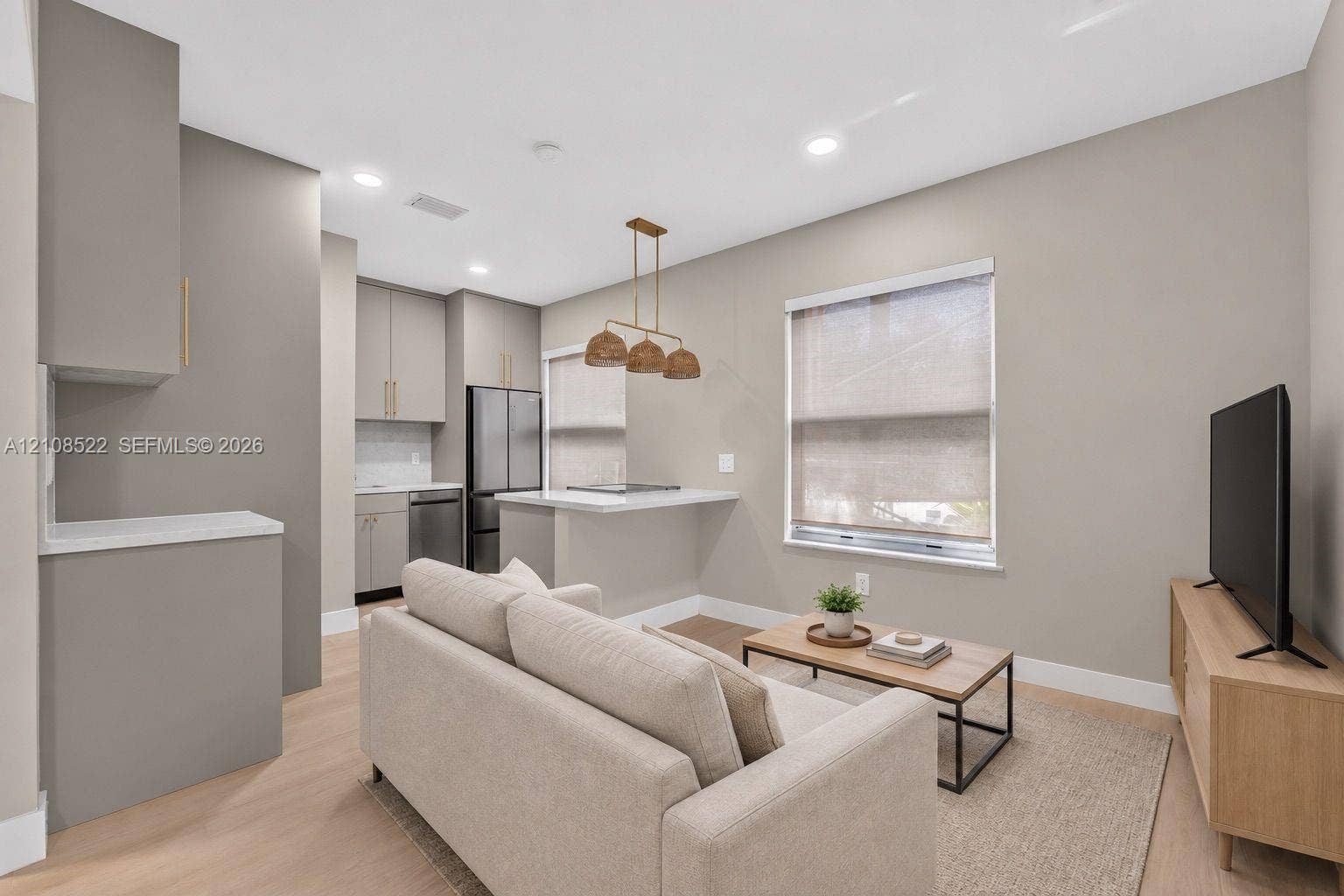 Open-concept area featuring light wood-finish flooring, recessed lighting, neutral wall palette, a multi-pendant light fixture, and kitchen cabinetry with stainless steel appliances