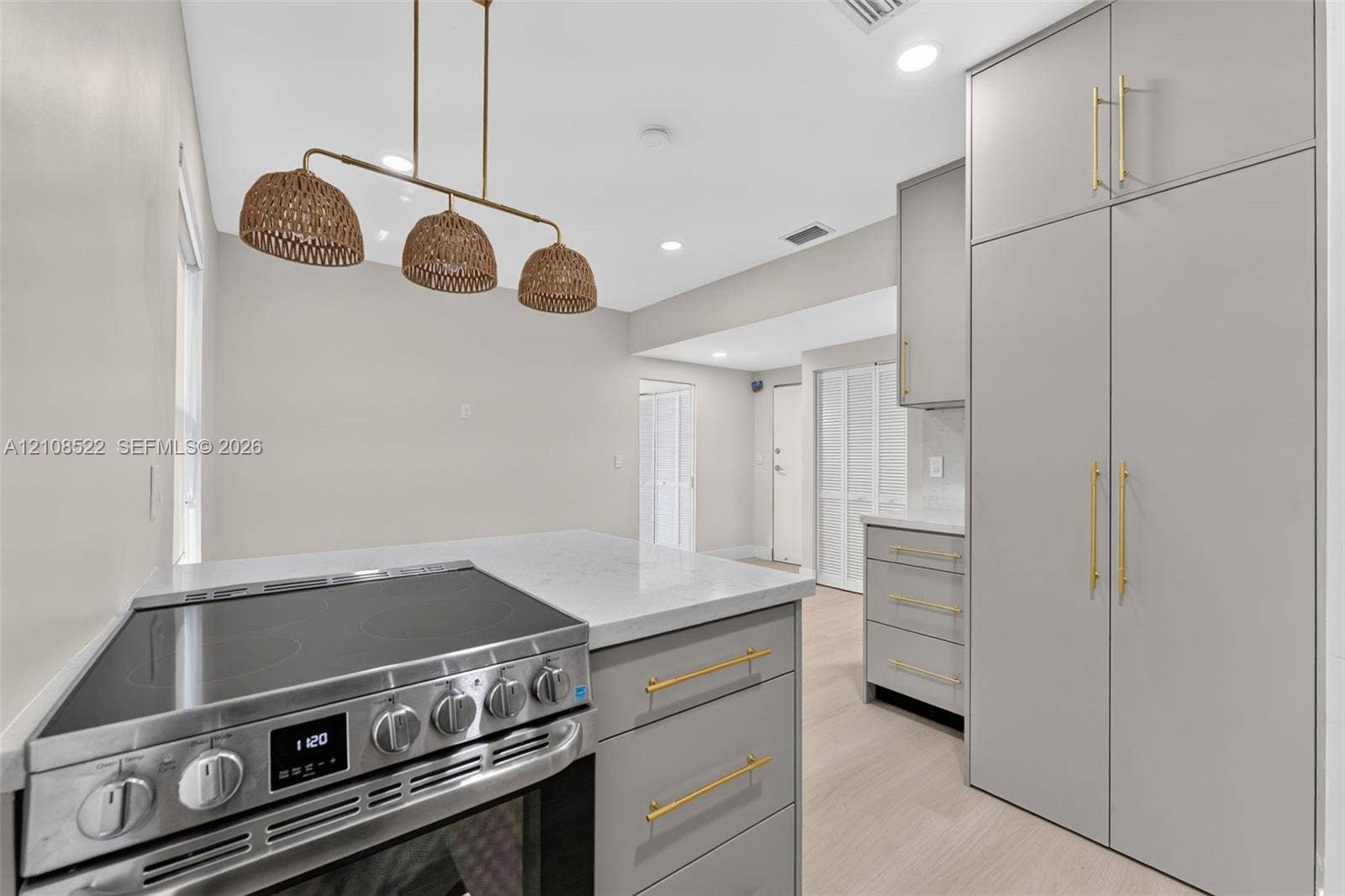 Kitchen featuring matte gray cabinetry with gold-toned hardware, quartz countertops, a stainless steel electric range, and a triple-pendant woven light fixture over wood-finish flooring