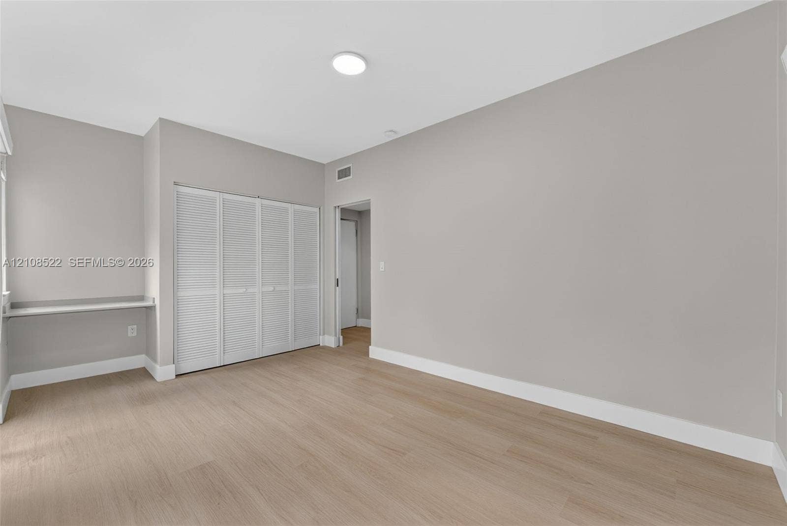 Room featuring wood-finish flooring, neutral wall paint, a built-in wall desk, and a four-panel louvered closet door